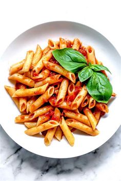 a white bowl filled with pasta and sauce on top of a marble countertop next to a green leafy garnish