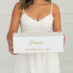 a woman holding a box with the word grace written on it in gold foil and white