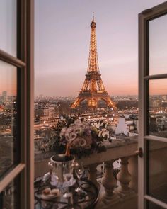 the eiffel tower is lit up at night from an open window with a view of the city below