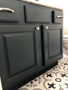 a white toilet sitting next to a dark green cabinet in a bathroom on top of a tiled floor