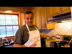 a man standing in a kitchen next to a pot on the stove and wearing an apron