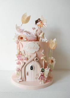 a pink cake decorated with flowers and fairy figurines on it's side