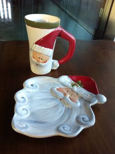 a ceramic cup and saucer on a table with a santa clause mug next to it