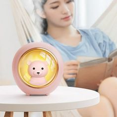 a woman reading a book while sitting in a hammock with a teddy bear alarm clock