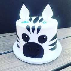 a zebra themed cake with blue eyes and ears on top of a wooden table in front of a black background