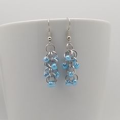 a pair of silver and light blue glass bead earrings on a white cup holder