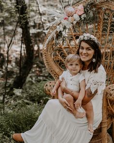 a woman holding a baby sitting in a wicker chair with flowers on her head