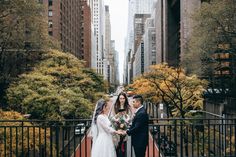 a bride and groom standing in the middle of a street with tall buildings behind them