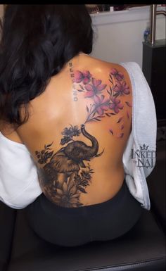 the back of a woman's body with an elephant and flowers tattoo on it