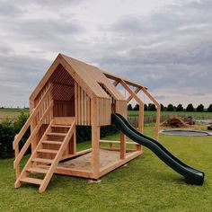 a wooden play house with a slide in the grass