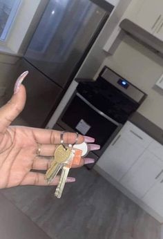 a woman's hand holding three keys in front of an oven and stove top