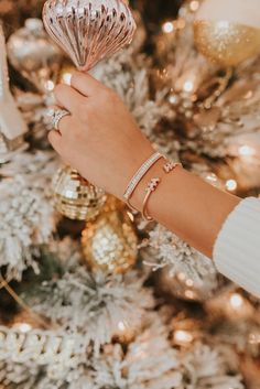 a close up of a person's hand holding a christmas ornament in front of a tree