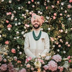 a man wearing a turban standing in front of pink flowers and greenery