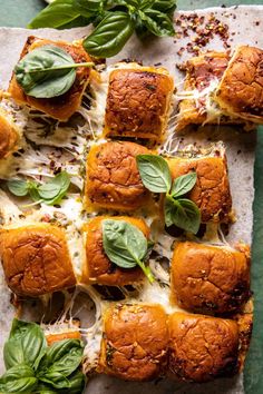 small sandwiches with cheese and spinach on a sheet of wax paper next to basil leaves