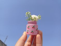 a hand holding a small pink jar with flowers in it