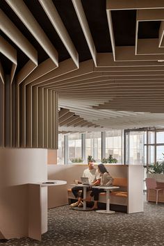 two people are sitting at a table in an office with large windows and wooden slats on the ceiling