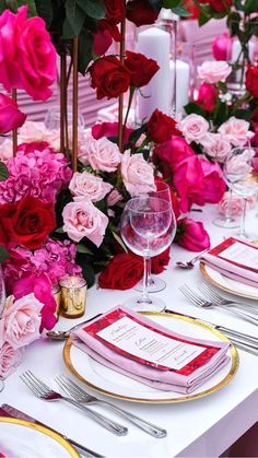 the table is set with pink and red flowers, gold rimmed place settings, and silverware