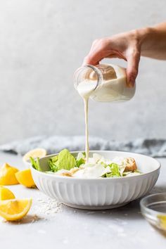 someone pouring dressing into a white bowl filled with salad and lemons on the side