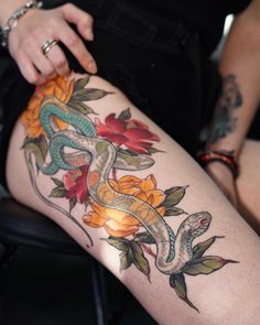 a woman with tattoos on her thigh and arm is holding onto a snake that has been wrapped around roses