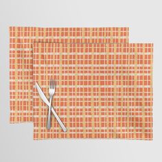 an orange and white place mat with two forks next to each other on top of it