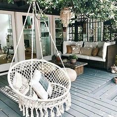 a white hanging chair sitting on top of a wooden floor next to a patio area