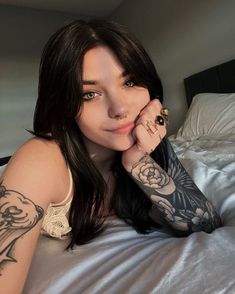 a woman laying on top of a bed with tattoos on her arms and arm,