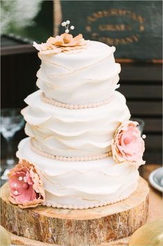 a three tiered wedding cake with pink flowers on the top and bottom, sitting on a tree stump