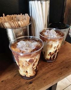 two glasses filled with ice cream sitting on top of a wooden table next to drinks