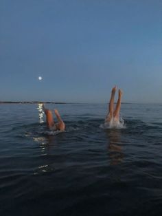 two people are swimming in the ocean under a moonlit sky with their legs up