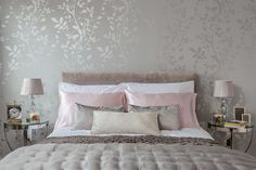 a bed with pink and white pillows in a bedroom next to a wallpapered wall