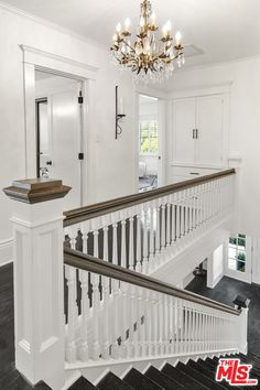 a white staircase with chandelier and black flooring in a home that is for sale