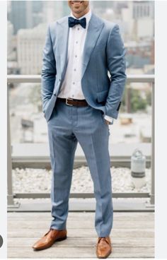 a man in a blue suit and bow tie is standing on a wooden deck with his hands in his pockets