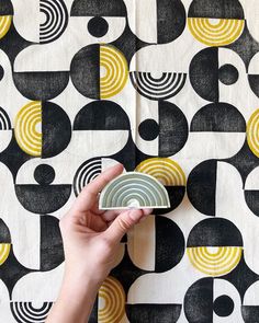 a hand is holding a small plate on a wallpapered surface with black, yellow and white circles