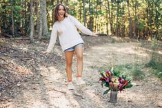 a woman walking down a dirt road next to a vase with flowers on the ground