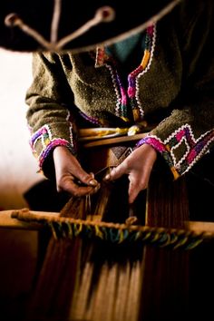 a person is weaving on a loom with their hands and colors in the background