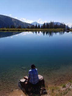 a man sitting on top of a rock next to a lake