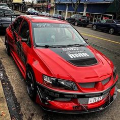 a red car parked on the side of a road next to a street with cars