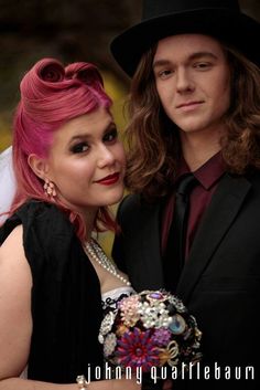 a man with pink hair and a woman in black dress posing for a photo together