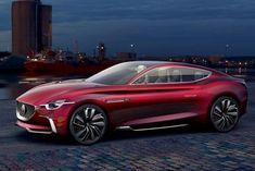 a red car parked in front of a large body of water next to tall buildings