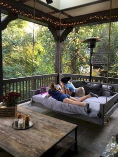 two people sitting on a porch swing bed with lights strung from the ceiling and trees in the background