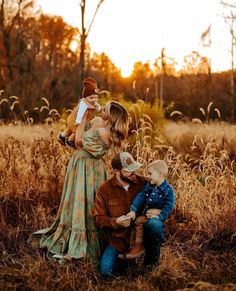 a woman and two boys are sitting in the grass with their mom holding her baby