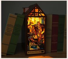 a miniature house made out of books on top of a wooden table next to a lamp