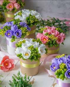 small flower pots with flowers in them sitting on a table next to ribbons and greenery