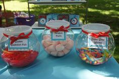 there are three glass jars with candy in them on the blue tablecloth at an outdoor party