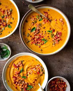 three white bowls filled with carrot soup and garnished with green leafy toppings