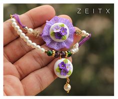 a hand holding a purple flower and pearl bead necklace with pearls on it's end