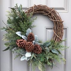 a wreath with pine cones and greenery is hanging on the front door for christmas