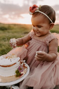 a baby girl in a pink dress holding a cake