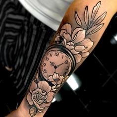 a person with a tattoo on their arm has a clock and flowers tattooed on it