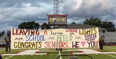 a group of people standing on top of a football field holding up a large sign